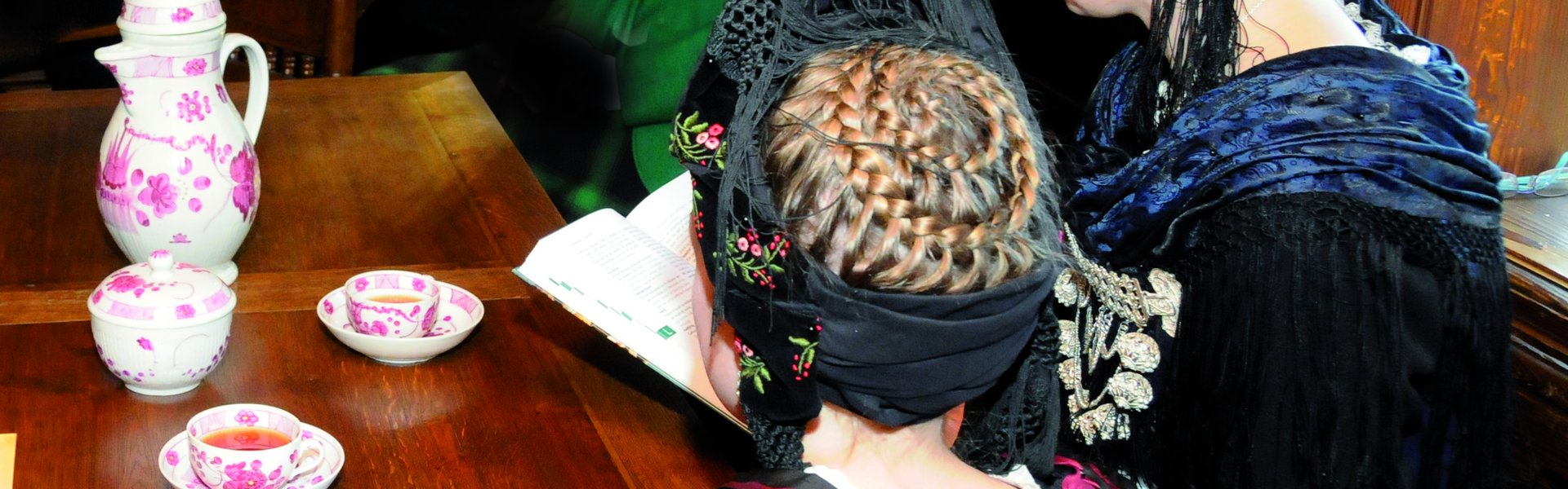 Es sind zwei Frauen in friesischer Tracht zu sehen, die Teetassen vor sich stehen haben.