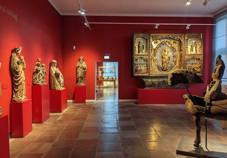 Im Museumsberg gibt es einen Ausstellungsraum zu kirchlicher Kunst. Auf Sockeln stehen Figuren und ein großer Flügelalter aus Holz. In der Mitte des Raumes steht eine weitere Holzskulptur. Die Wände sind rot gestrichen.