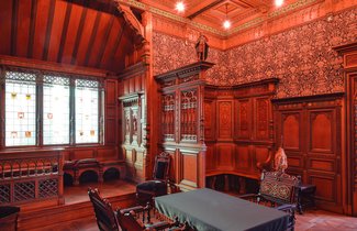 In einem Raum mit dunklem Holz an den Wänden steht ein Tisch mit Stühlen. Es handelt sich hierbei im das Pariser Zimmer, das von Heinrich Sauermann für die Weltausstellung im Jahr 1900 entworfen wurde.