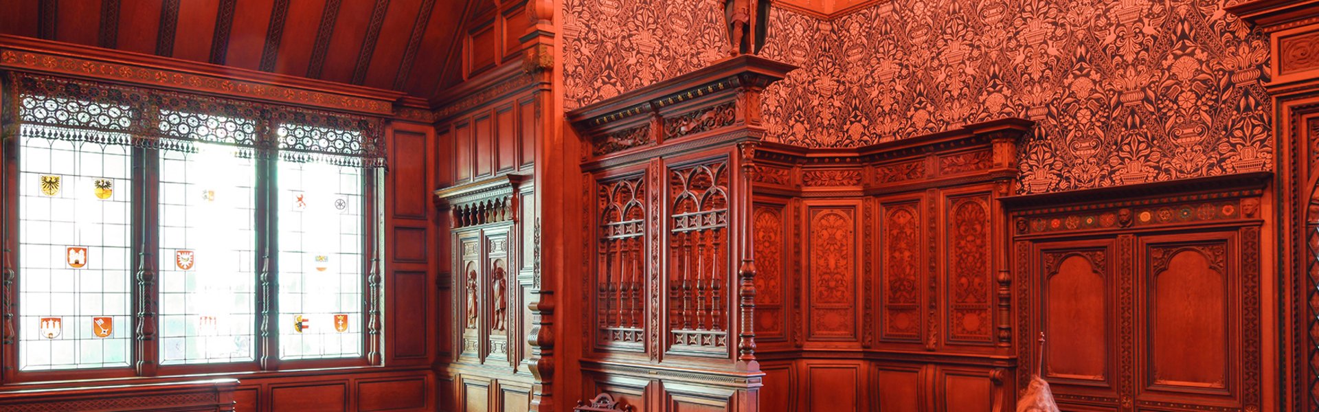 In einem Raum mit dunklem Holz an den Wänden steht ein Tisch mit Stühlen. Es handelt sich hierbei im das Pariser Zimmer, das von Heinrich Sauermann für die Weltausstellung im Jahr 1900 entworfen wurde.