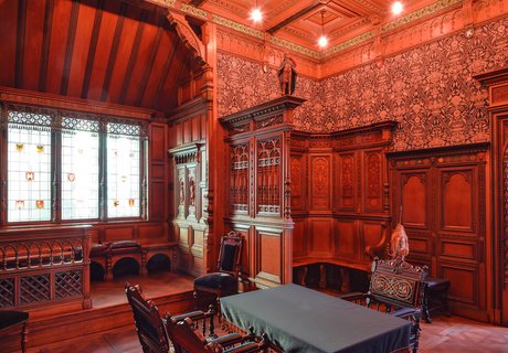 In einem Raum mit dunklem Holz an den Wänden steht ein Tisch mit Stühlen. Es handelt sich hierbei im das Pariser Zimmer, das von Heinrich Sauermann für die Weltausstellung im Jahr 1900 entworfen wurde.