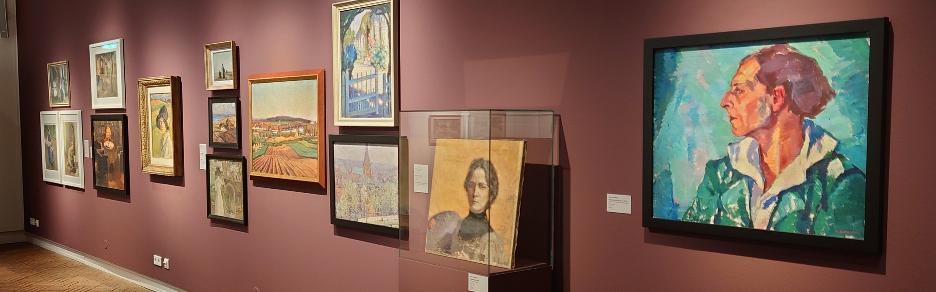 Es ist ein Raum zu sehen, in dem mehrere Bilder einer Ausstellung hängen.