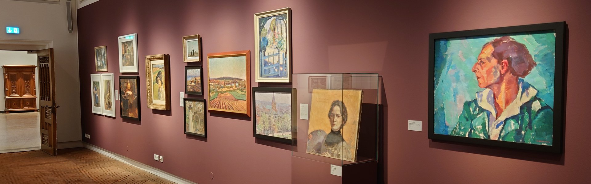 Es ist ein Raum zu sehen, in dem mehrere Bilder einer Ausstellung hängen.