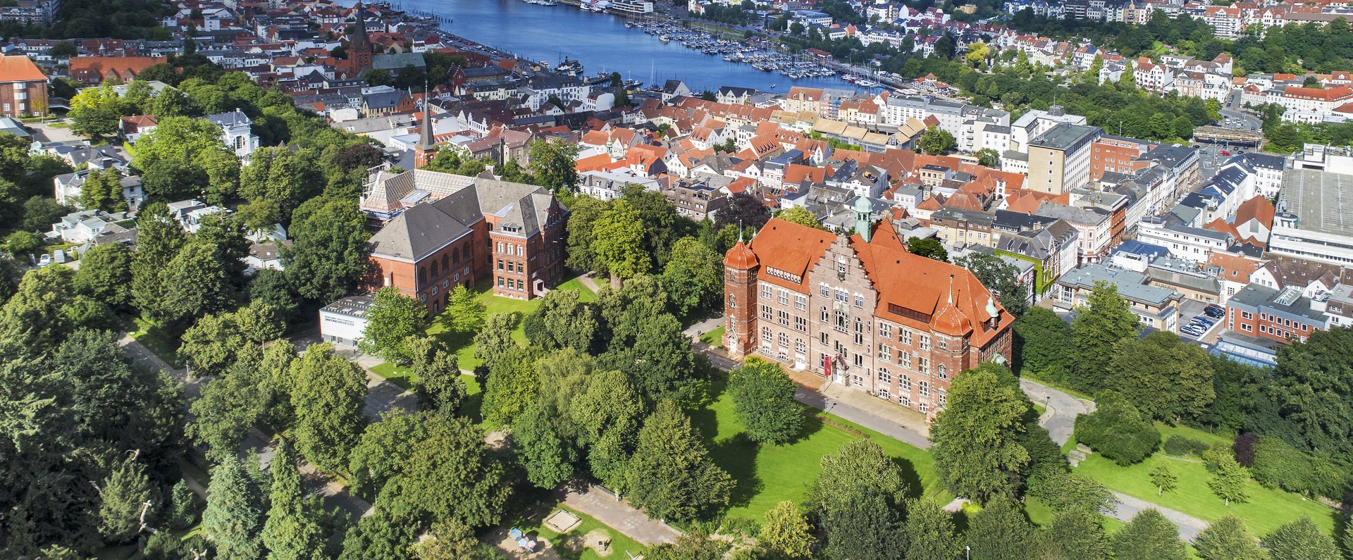 Das Heinrich-Sauermann-Haus und das Hans-Christiansen-Haus sind die beiden großen Häuser vorne. Zusammen sind sie der Museumsberg Flensburg. Das Foto wurde von weit oben gemacht, deshalb sind noch andere Häuser und die Flensburger Förde zu sehen. 