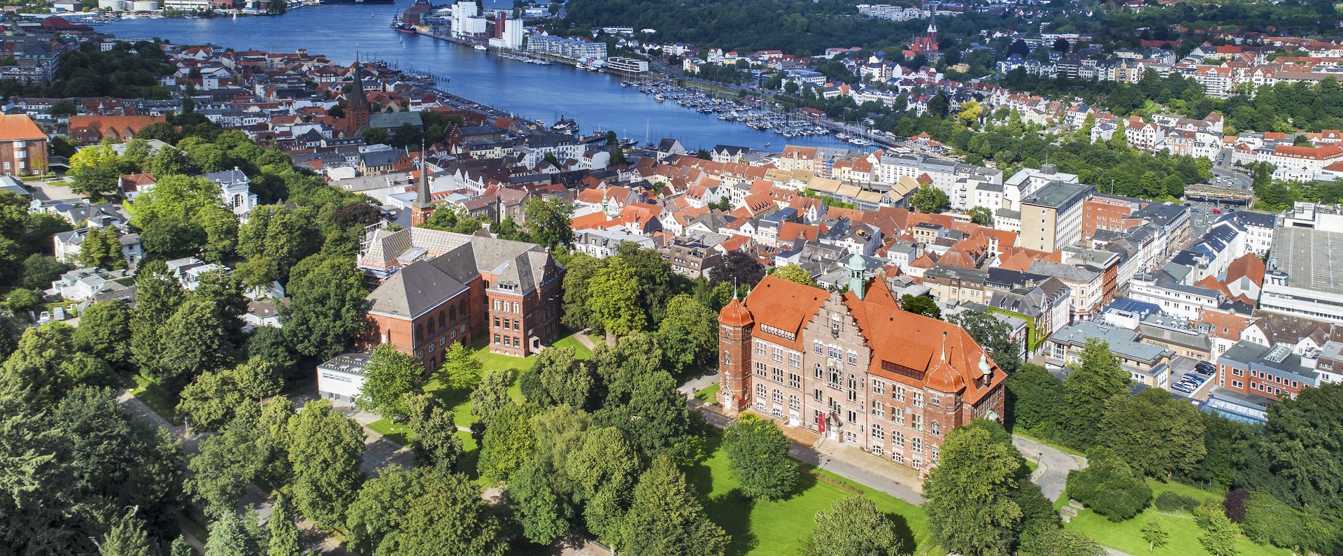 Das Heinrich-Sauermann-Haus und das Hans-Christiansen-Haus sind die beiden großen Häuser vorne. Zusammen sind sie der Museumsberg Flensburg. Das Foto wurde von weit oben gemacht, deshalb sind noch andere Häuser und die Flensburger Förde zu sehen. 