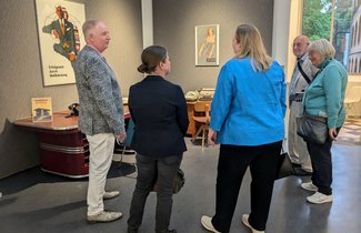 In einem Ausstellungsraum im Museumsberg hängen verschiedene Kunstwerke. Bei einer Führung erklärt eine Mitarbeiterin mehreren Menschen die Kunst.