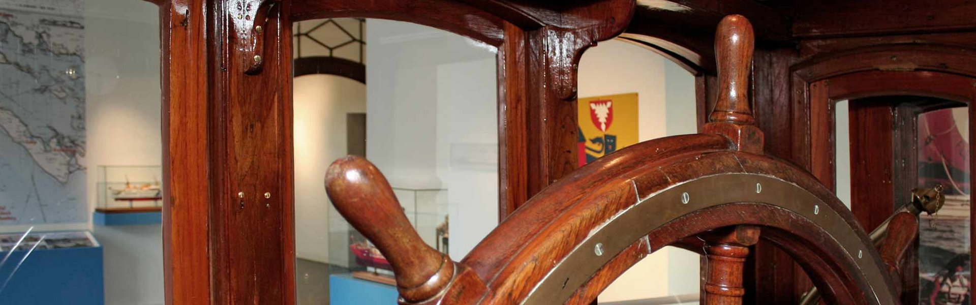 Das Foto zeigt den Blick aus dem Steuerhaus HABICHT in die Ausstellung FÖRDESCHIFFAHRT im Flensburger Schifffahrtsmuseum. Im Steuerhaus ist ein großes Ruder bzw. Steuerrad mit dem das Schiff früher gesteuert worden ist.