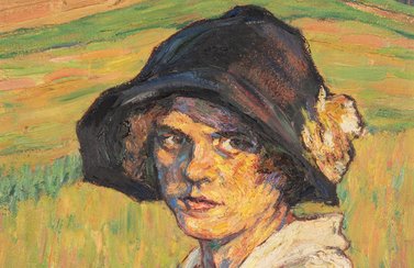 Eine junge Frau mit braunem Hut steht vor einem Feld. Es handelt sich um ein Bild von Emmy Gotzmann.